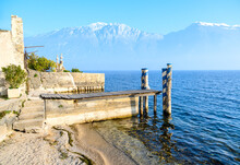An Old Wooden Jetty On The Lake, Next To An Orange Orchard And Snowy Mountains On The Horizon