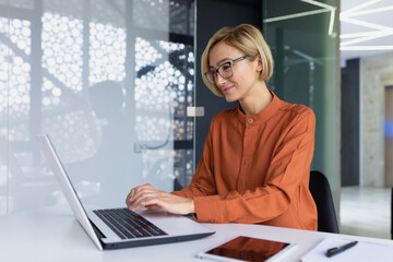 beautiful young businesswoman inside office working with laptop, blonde with short hair typing on ke