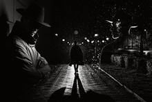 Man Spy Agent Detective In Raincoat And Hat In Night City With Rain In Style Of Film Noir. Collage With Dark Male Silhouettes