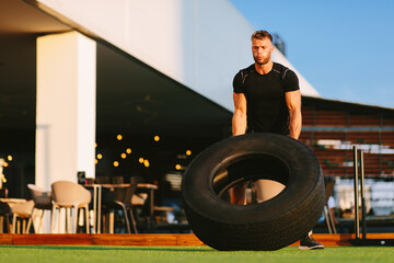 Wall Mural - Handsome young man working out in an outdoor gym and flipping tire