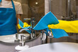 © Volha - Close-up of a woman 's hand in yellow rubber gloves wiping the faucet with a blue cleaning cloth in a modern bathroom. Concept of professional cleaning