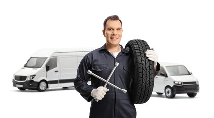 Wall Mural - Auto mechanic posing in front of vans and holding a tire and a wrench tool