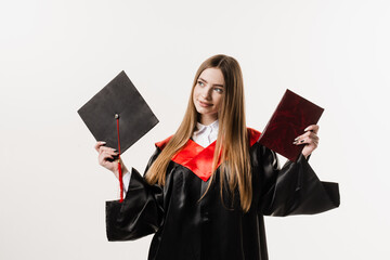 Wall Mural - Graduate girl master degree in black graduation gown is holding diploma and cap in hands on white background. Attractive young woman graduated from college.