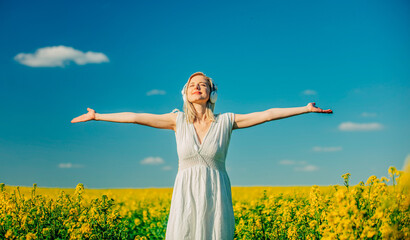 Canvas Print - woman in dress with headphones in rapeseed field