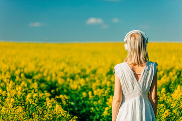 Wall Mural - woman in dress with headphones in rapeseed field