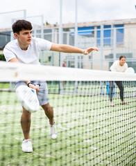 Wall Mural - Young European male player serving ball during training padel in court outdoors in spring