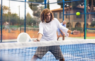 Wall Mural - Portrait of active adult man enjoying friendly padel tennis match at outdoors court