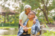 © NanSan - Elderly couple husband and wife happy asian people giving love and care Wheelchair in the park relaxing in spring, relaxing and walking outside at the park.