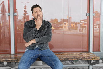 Canvas Print - Sleepy man yawning at public transport stop outdoors. Space for text