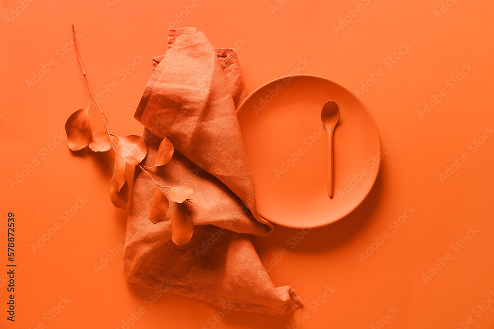 Plate with spoon, napkin and plant branch on orange background