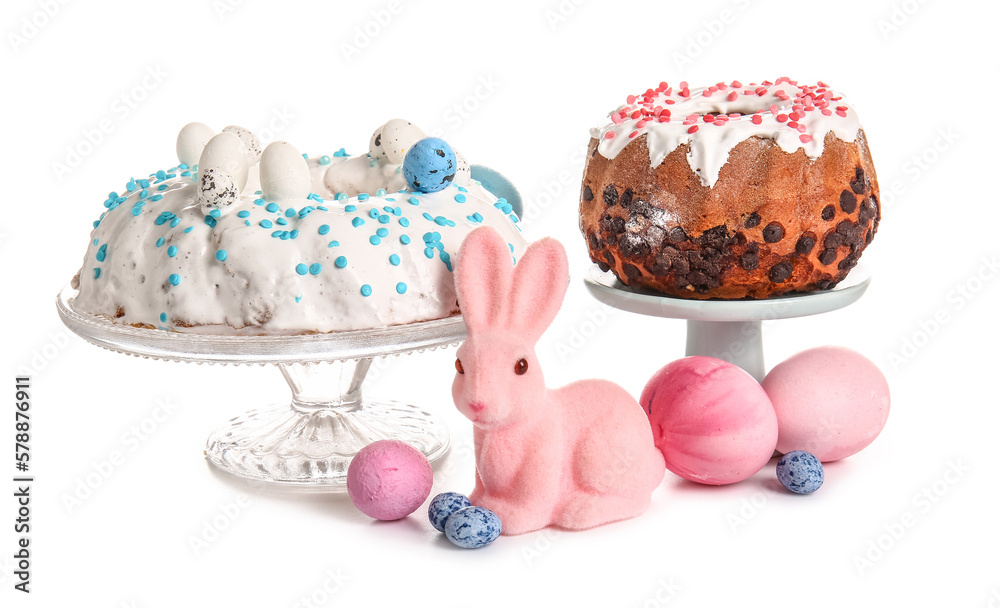 Dessert stands with tasty Easter cakes, eggs and toy bunny on white background