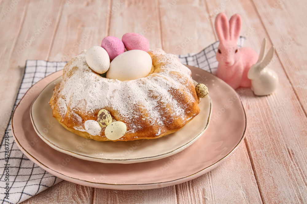 Plate with tasty Easter cake, eggs and bunnies on light wooden background