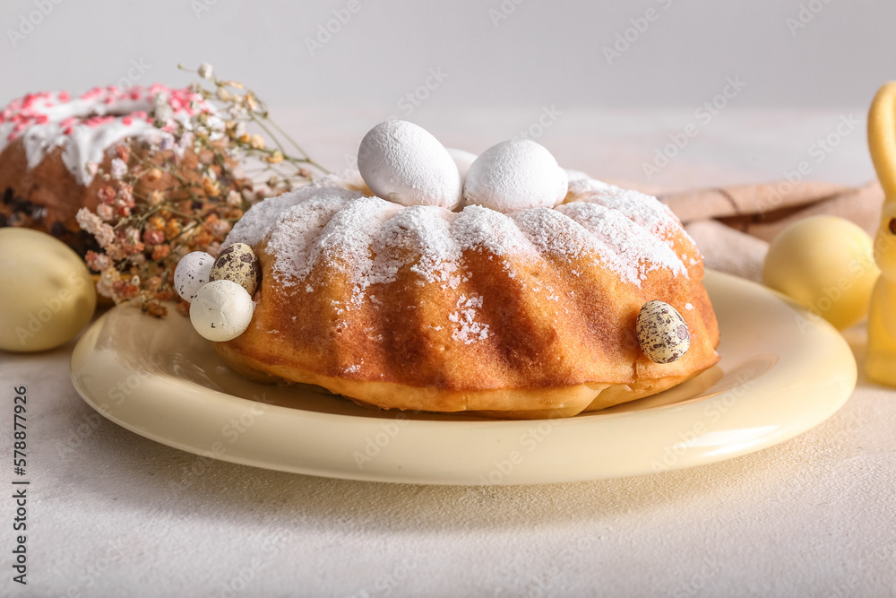 Plate with tasty Easter cake, eggs and beautiful gypsophila flowers on grey table
