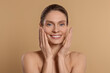 © New Africa - Woman massaging her face on beige background