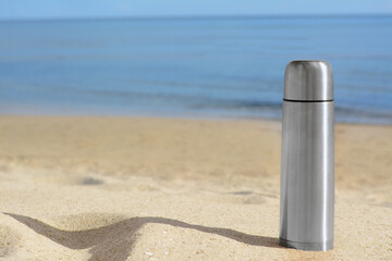 Canvas Print - Metallic thermos with hot drink on sandy beach near sea, space for text