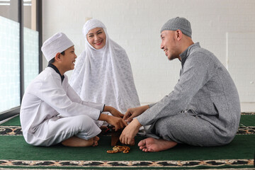 Wall Mural - Cheerful muslim family with children reading Quran together and discuss about Islam after praying together at the mosque