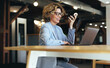 © Jacob Lund - Woman talking on a phone call while working on a laptop in a coworking space