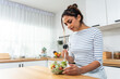 © Kawee - Caucasian young woman eating healthy green salad in kitchen at home.