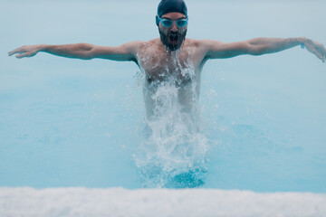 Fit swimmer male training swim in open winter swimming pool with fog. Geothermal outdoor spa health concept.