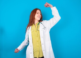 Profile photo of excited young doctor woman wearing medical uniform over blue background good mood raise fists screaming rejoicing overjoyed basketball sports fan supporter