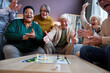 © Seventyfour - Multiethnic group of excited senior people playing board games at retirement home and celebrating win