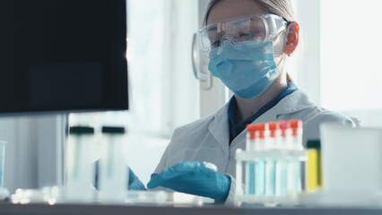 Aufkleber - A female researcher sits at a workplace in a laboratory, behind a personal computer monitor. Against the background research statistics. Pharmaceutical medical worker in protection works at keyboard.