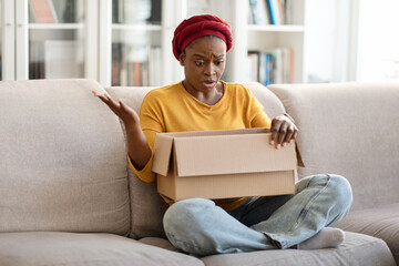 Angry irritated black woman unpacking parcel at home