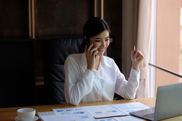 Smiling beautiful young Asian businesswoman ready to press the phone Talking on the mobile phone in the office with a happy smile.