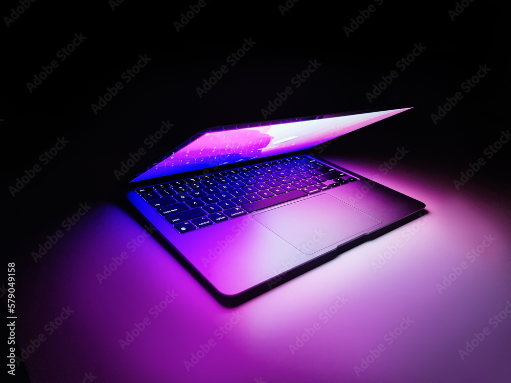 Half Theme Computer Laptop with half lid open on a table lit with colorful purple and blue ...