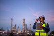Engineer wearing safety uniform and helmet looking detail tablet on hand with oil refinery factory at night time background.	
