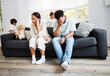 Sad, unhappy and stressed parents sitting on a couch near their children at home after an argument. Frustrated, tired and annoyed mom and dad are angry at hyperactive, noisy and naughty kids