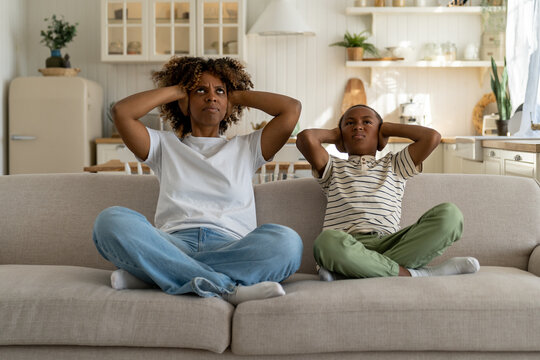 dissatisfied annoyed stressed african american woman mom and child son sitting on crossed legs, disp