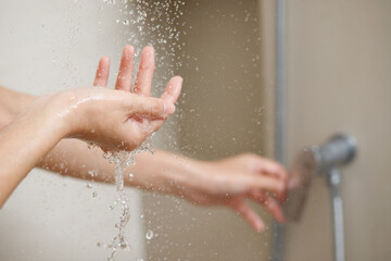 A woman uses hand to measure the water temperature from a water heater before taking a shower