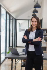 Poster - A stylish white businesswoman in a black suit standing inside the office in hands with a mobile phone, tablet, and laptop waiting for customers to contact, business people concept.