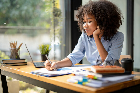 black woman sitting in front of her considering work, office work business woman sitting thinking wo