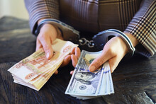 Women's Handcuffed Hands Hold Dollars On A Dark Wooden Background
