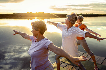 Group of senior woman doing yoga exercises by the lake.