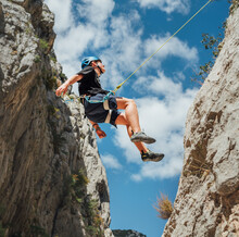 Climber Teenage Boy In Protective Helmet Jumping On Vertical Cliff Rock Wall Using Rope Belay Device, Climbing Harness In Paklenica Canyon In Croatia. Active Extreme Sports Time Spending Concept