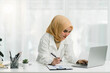 © PRIME STOCK LAB - A beautiful Muslim businesswoman is using a digital laptop at her desk in a modern office.