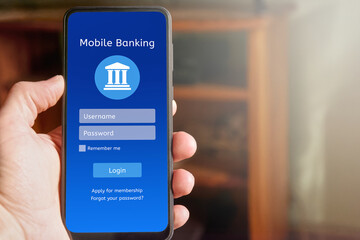 Male hand holding mobile phone with online banking app interface on the screen, login page with username and password boxes, with copy space for text in the background