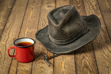 Sticker - weathered outback oilskin hat with metal enamel mug of tea on a rustic wooden table