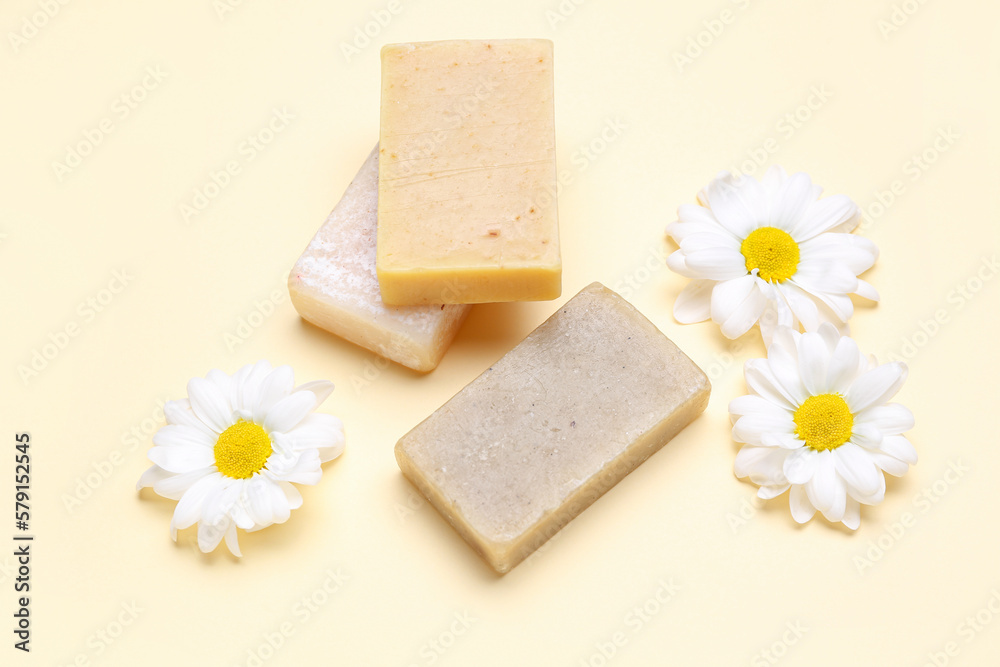 Soap bars and chamomile flowers on color background