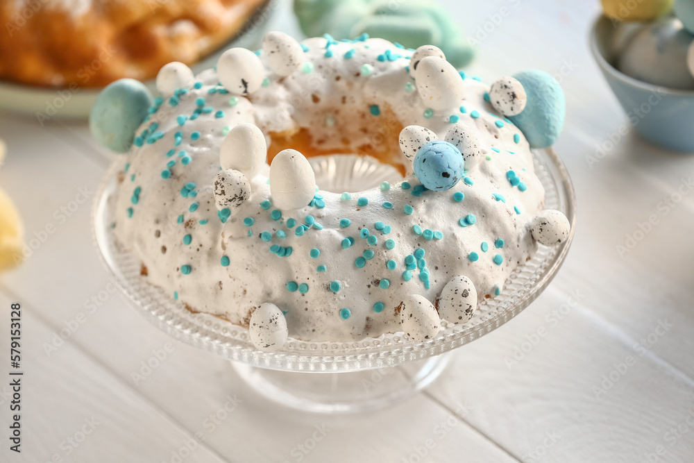 Dessert stand with tasty Easter cake and painted eggs on white wooden table