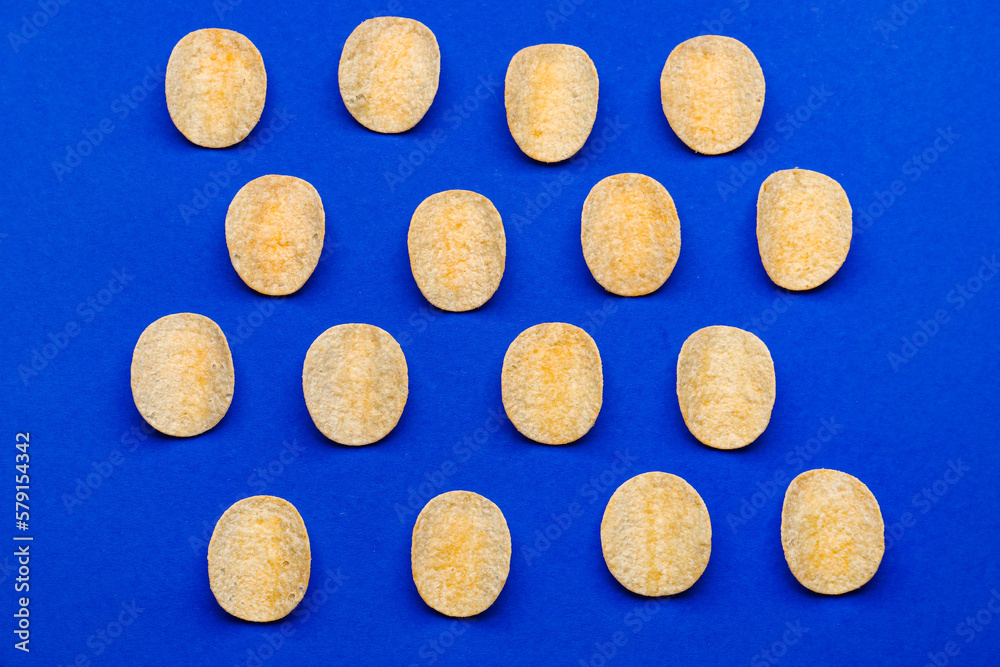 Many delicious potato chips on blue background