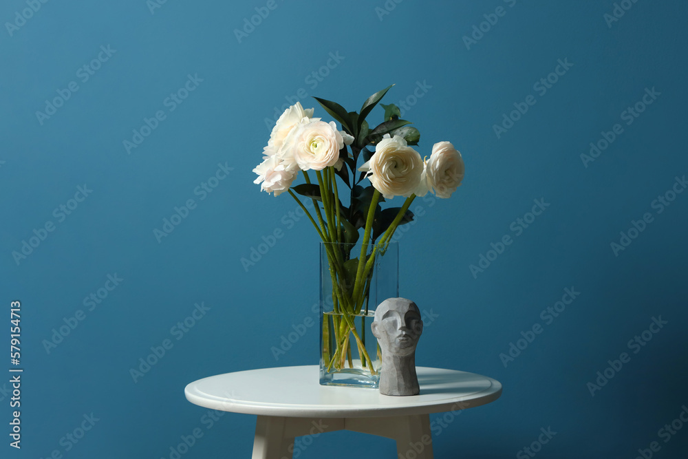 Vase with ranunculus flowers and decor on table near blue wall
