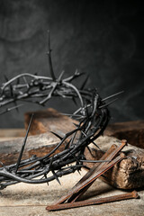 crown of thorns, nails and cross on wooden table, closeup
