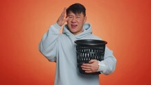 Asian Man Taking Off, Throwing Out Glasses Into Bin After Medical Vision Laser Treatment Therapy Surgery, Looking Smiling At Camera. Handsome Chinese Guy Isolated Alone On Orange Studio Background