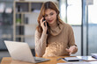 © David - Attractive successful young business Asian woman in striped blouse working in modern office, making phone call to potential client, having nice conversation, sitting at desk in front of open laptop