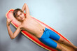 Smiling boy in swim jammers lying down on his surfboard