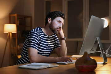 Poster - Home workplace. Tired man working with computer at wooden desk in room at night